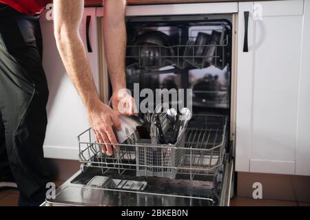 Primo piano di un uomo Caricamento lavastoviglie in cucina. Lavori domestici Foto Stock