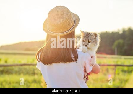 Bambina in cappello con gatto grigio soffice tra le braccia. Bellissimo tramonto paesaggio sfondo paese