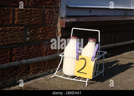 Cassa del latte sul viale di accesso dalla porta anteriore di una casa con consegna del latte a domicilio, due pinte di latte parzialmente scremato in bottiglie di vetro riutilizzabili. Foto Stock