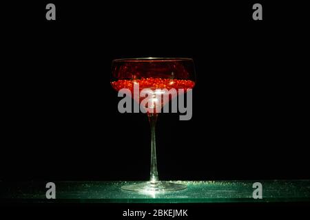 Bicchiere singolo in stile martini illuminato con caviale d'acqua rosso luminoso in stile cocktail. Arte della vetreria Foto Stock