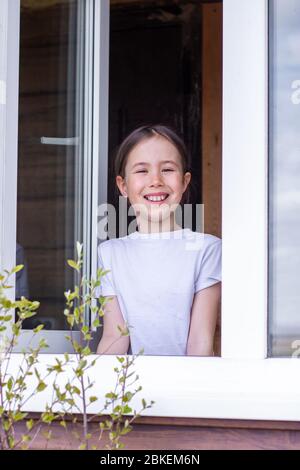 La bambina guarda fuori dalla finestra del suo appartamento e gode la primavera Foto Stock