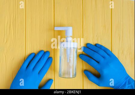 Il flacone igienizzante per le mani e le mani con guanti blu si avvicinano. Richiedere la disinfezione delle mani. Stop concetto di coronavirus. Uso di gel antibatterico per le mani durante Foto Stock