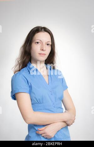 Ritratto studio a metà coscia di giovane donna piuttosto a capelli lunghi in abito blu a manica corta isolato su bianco. Sembra calmo e serio guardando a. Foto Stock