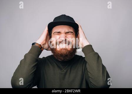 Il giovane ha mal di testa e tiene le mani strette sulla testa con gli occhi chiusi su sfondo bianco. Foto Stock