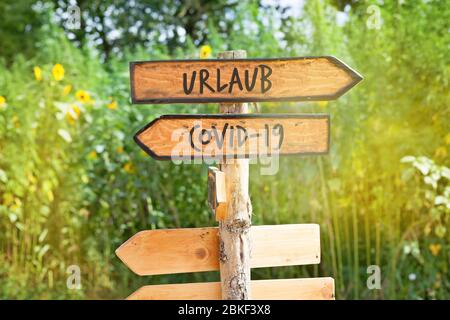 Cartello di direzione in legno con le parole tedesche vacanza e Covid-19 (Urlaub, Covid-19) Foto Stock