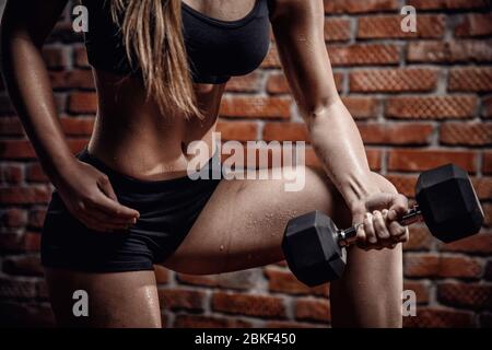 Fitness giovane donna treni per pompare i muscoli delle mani con manubri. Foto Stock