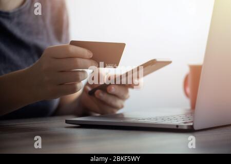Primo piano delle mani che tengono la carta di credito nera e digitano sulla tastiera del laptop. Concetto di banking o pagamento online Foto Stock