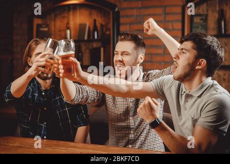 Uomini bearded, vecchi amici si divertono al bar notturno insieme. Gridando, si aggraffano bicchieri di birra. Concetto tempo felice, gioventù spensierata, fine settimana Foto Stock