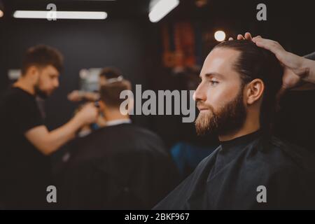 Uomo seduto in poltrona barbershop, barbiere si sta preparando a tagliare i capelli. Foto Stock