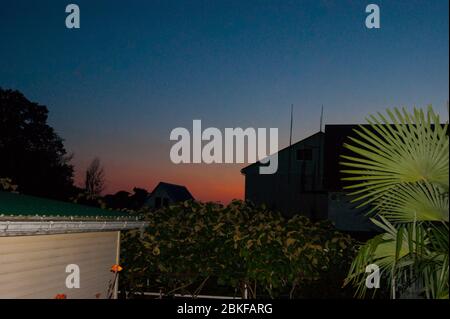 Tramonto nei tropici - un cielo blu scuro con una striscia di rosso tramonto sullo sfondo di case, piante e palme. Viaggio estivo serale turismo caucasico montagna Foto Stock