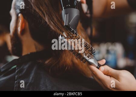 Barber rende l'acconciatura dei capelli all'uomo con asciugacapelli e pettine. Foto Stock