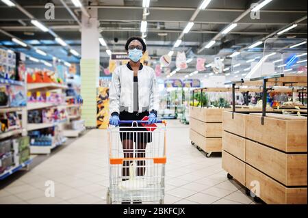 Donna africana che indossa la maschera medica monouso e guanti shopping in supermercato durante lo scoppio della pandemia del coronavirus. Tempo epidemico. Foto Stock