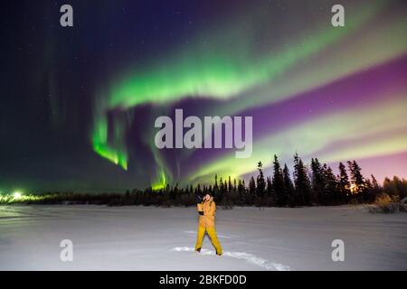 Uomo viaggiatore in giacca gialla con macchina fotografica sullo sfondo dell'aurora boreale. Effetto sfocatura soft focus Foto Stock