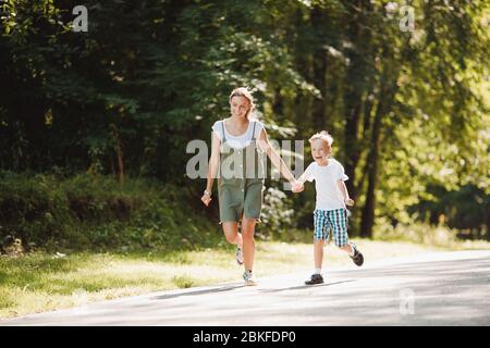 Fratello minore e sorella maggiore corrono intorno al parco, tenendo le mani, divertendosi, ridenti, sorridenti. Concetto famiglia felice. Foto Stock