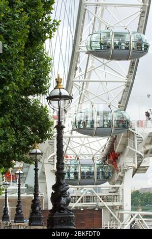 Un primo piano di una parte del London Eye o della ruota Millenium in una giornata nuvolosa a Londra con vecchi lampioni in primo piano. Foto Stock