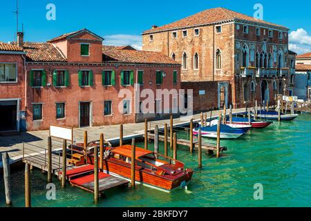 Motoscafi sul canale di fronte alla strada stretta e vecchie case tipiche sull'isola di Murano in Italia. Foto Stock