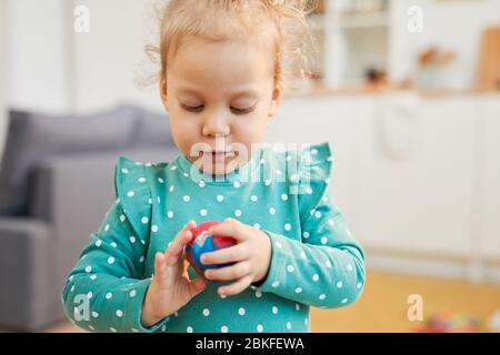 Bambina caucasica che indossa abiti a pallini turchesi a pallina di argilla modellante, ritratto orizzontale girato Foto Stock