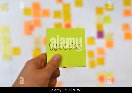 Una mano sta tenendo un adesivo giallo di successo e c'è un bordo Kanban di metodologia agile sullo sfondo, che è una tendenza in sviluppo in ESSO Foto Stock