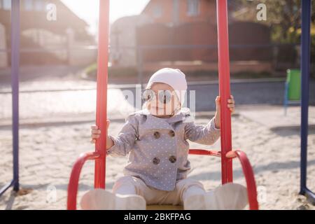 Adorabile bambina sul swing set nel parco giochi. Ragazza felice poco divertirsi. Una ragazza e hulf anno Foto Stock