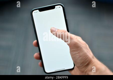 Una mano tiene un iPhone X Apple su uno sfondo piano. IPhone X ha uno sfondo bianco vuoto sullo schermo. La foto è scattata a Istanbul, Foto Stock