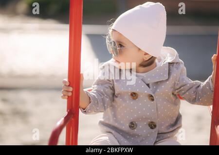 Adorabile bambina sul swing set nel parco giochi. Ragazza felice poco divertirsi. Una ragazza e hulf anno Foto Stock