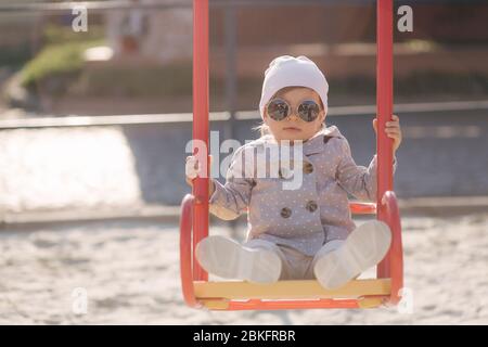 Adorabile bambina sul swing set nel parco giochi. Ragazza felice poco divertirsi. Una ragazza e hulf anno Foto Stock