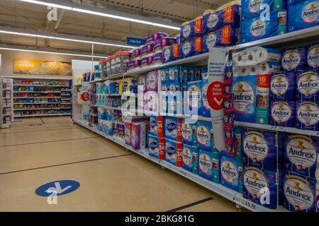 Scaffali finalmente pieni di rotolo di gabinetto alla fine di una giornata nel supermercato Tesco mostrando due metri di distanza sociale marcatori e un senso freccia sistema su t. Foto Stock