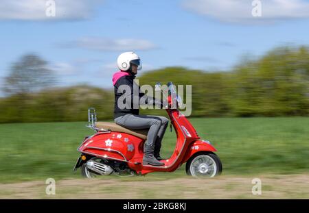 Kiel, Germania. 04 maggio 2020. In tempo soleggiato, una donna guida il suo scooter rosso Vespa 125 cc lungo una strada sterrata indossando indumenti di sicurezza, casco e guanti. Dal 01.01.2020, i titolari di una patente di guida non hanno più bisogno di una patente di guida per motocicli separata. Sono sufficienti solo 5 ore di guida e 4 ore teoriche per poter guidare veicoli a due ruote fino a 125 ccm. Credit: Axel Heimken/dpa/Alamy Live News Foto Stock