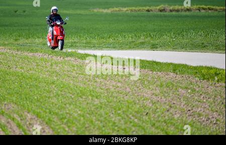 Kiel, Germania. 04 maggio 2020. In tempo soleggiato, una donna guida il suo scooter rosso Vespa 125 cc lungo una strada sterrata indossando indumenti di sicurezza, casco e guanti. Dal 01.01.2020, i titolari di una patente di guida non hanno più bisogno di una patente di guida per motocicli separata. Sono sufficienti solo 5 ore di guida e 4 ore teoriche per poter guidare veicoli a due ruote fino a 125 ccm. Credit: Axel Heimken/dpa/Alamy Live News Foto Stock