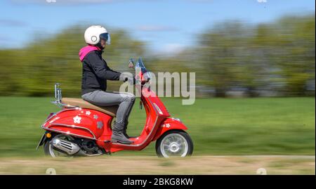 Kiel, Germania. 04 maggio 2020. In tempo soleggiato, una donna guida il suo scooter rosso Vespa 125 cc lungo una strada sterrata indossando indumenti di sicurezza, casco e guanti. Dal 01.01.2020, i titolari di una patente di guida non hanno più bisogno di una patente di guida per motocicli separata. Sono sufficienti solo 5 ore di guida e 4 ore teoriche per poter guidare veicoli a due ruote fino a 125 ccm. Credit: Axel Heimken/dpa/Alamy Live News Foto Stock