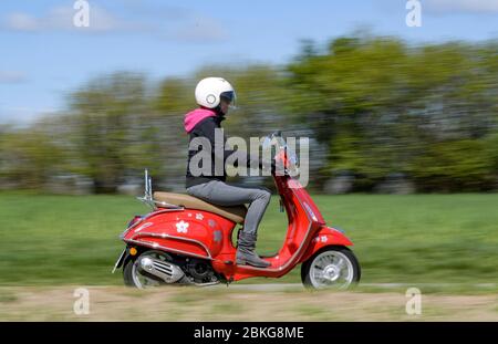 Kiel, Germania. 04 maggio 2020. In tempo soleggiato, una donna guida il suo scooter rosso Vespa 125 cc lungo una strada sterrata indossando indumenti di sicurezza, casco e guanti. Dal 01.01.2020, i titolari di una patente di guida non hanno più bisogno di una patente di guida per motocicli separata. Sono sufficienti solo 5 ore di guida e 4 ore teoriche per poter guidare veicoli a due ruote fino a 125 ccm. Credit: Axel Heimken/dpa/Alamy Live News Foto Stock