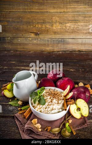Colazione all'autunno o pranzo a base di porridge o budino con mela e spezie. Porridge di riso con cannella e mele rosse, su sfondo rustico in legno. Foto Stock