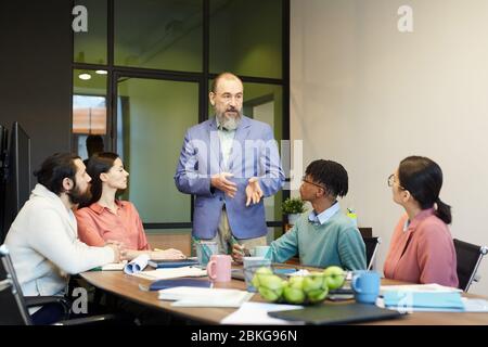 Uomo anziano moderno che indossa abiti eleganti davanti ai colleghi in sala per parlare di strategia aziendale, spazio per fotocopie Foto Stock