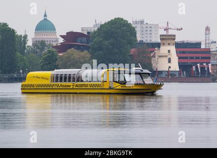 04 maggio 2020, Brandenburg, Potsdam: Il taxi d'acqua 3 viaggia sull'Havel o sul Tiefen See dal molo Parco Babelsberg passando la Chiesa Nikolai in direzione del Ponte Glienicke. Da pochi giorni le navi gialle sono nuovamente in servizio regolare tra Sacrow e Forsthaus Templin. Ci sono 13 stazioni e le biciclette possono essere prese a bordo. A causa del pericolo della corona, i passeggeri devono indossare una copertura per bocca e naso a bordo e mantenere una distanza minima di 1.5 metri. A causa delle restrizioni, le otto navi passeggeri della flotta bianca sono ancora situate nel porto tecnico in attesa di take-o Foto Stock