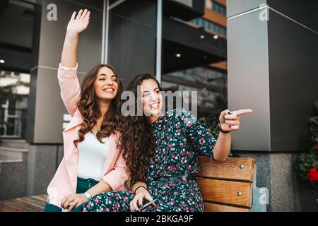 Immagine di un felice emotivo giovani amici graziose donne seduti all'aperto sulla strada della città e ondeggiare a qualcuno Foto Stock