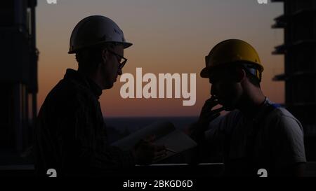 Lavoratori edili che hanno discussione al tramonto. Un fuma. Foto Stock