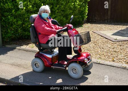 Una Signora su uno scooter mobile che indossa i DPI durante la chiusura a chiave Covid-19 Foto Stock