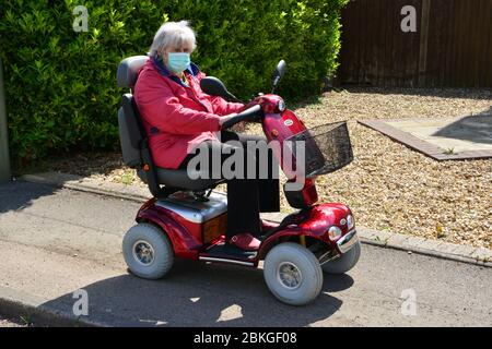 Una Signora su uno scooter mobile che indossa i DPI durante la chiusura a chiave Covid-19 Foto Stock