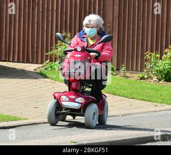 Una Signora su uno scooter mobile che indossa i DPI durante la chiusura a chiave Covid-19 Foto Stock