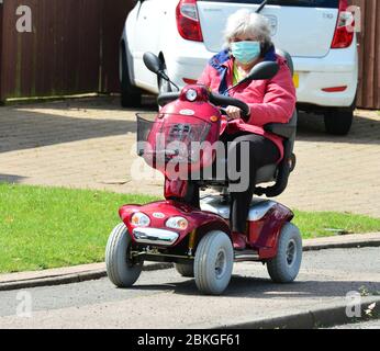 Una Signora su uno scooter mobile che indossa i DPI durante la chiusura a chiave Covid-19 Foto Stock