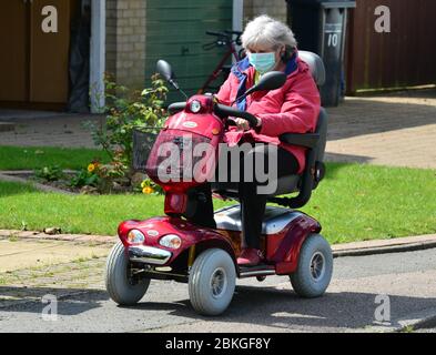 Una Signora su uno scooter mobile che indossa i DPI durante la chiusura a chiave Covid-19 Foto Stock