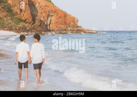 Indietro vista ritratto omosessuale giovane coppia asiatica a piedi con allegro insieme sulla spiaggia in estate, asia gay turismo in corso per il tempo libero e relax con Foto Stock