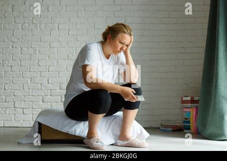 Sconvolto donna stressata che tiene il cellulare disgustato con il messaggio che ha ricevuto il background domestico. Triste aspetto umano espressione di viso emozione sensazione reazione Foto Stock