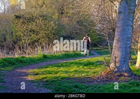 Una vista posteriore di un corridore maschile che si esercita su un sentiero nella campagna Shepperton Surrey UK Foto Stock