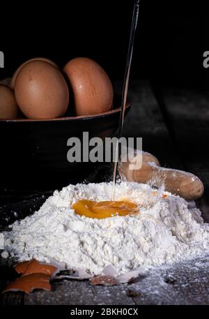 uovo che cade sulla farina, recipiente inferiore con uova e impastatrice di legno Foto Stock