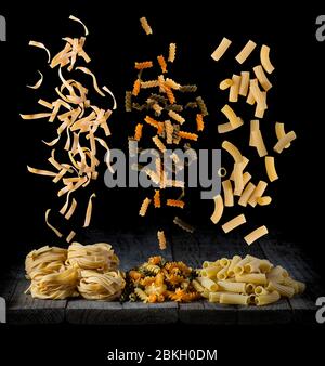 pasta fresca che cade in forme e colori diversi su un legno di fronte ad uno sfondo nero Foto Stock