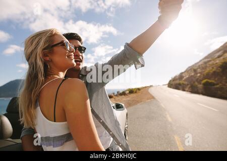 Bella giovane coppia appoggiata alla loro auto mentre facendo selfie in viaggio. Uomo e donna che catturano i ricordi durante il viaggio. Foto Stock
