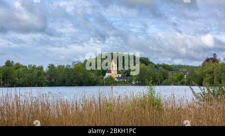 Lago Wessling con la chiesa 'Mariae Himmelfahrt' e alberi verdi e lussureggianti. Reed in primo piano. Luogo perfetto per escursioni giornaliere da Monaco. Formato panorama. Foto Stock