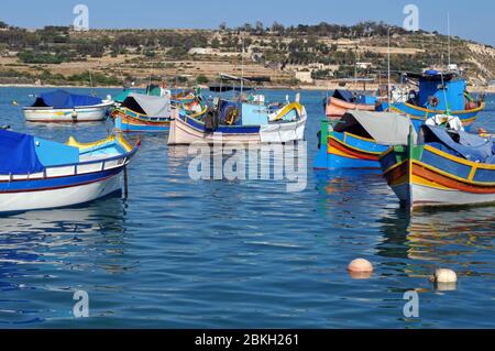 Le barche colorate della flotta di pescatori di Marsaxlokk, Malta, sono ormeggiate nel porto. Il villaggio tradizionale è popolare tra i turisti. Foto Stock