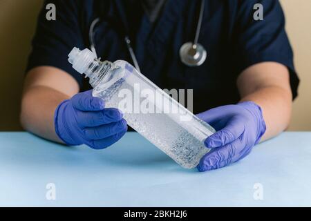 Un professionista medico con mani con guanti che tiene una bottiglia di igienizzante per le mani Foto Stock